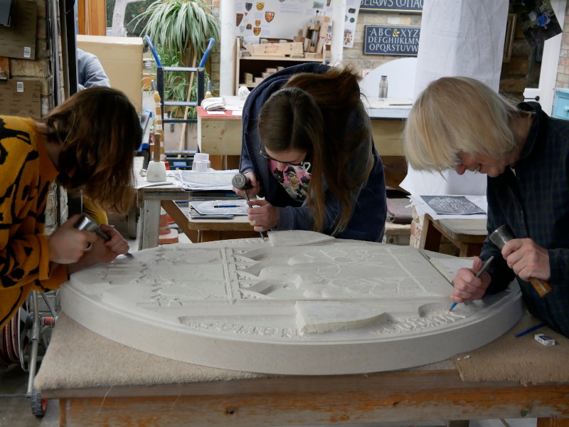 Three carvers work to establish levels on the stone